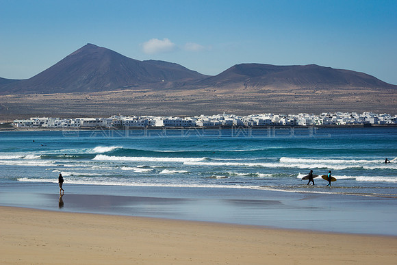 Surferos en la Playa de Famara con La Caleta al fondo - Teguise.