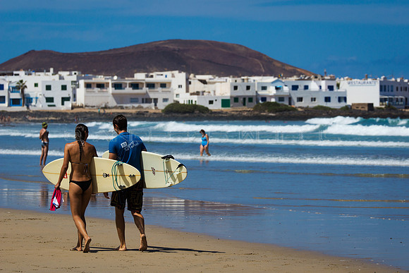 Una pareja de surfistas ante el pueblo costero de La Caleta de Famara, Teguise.